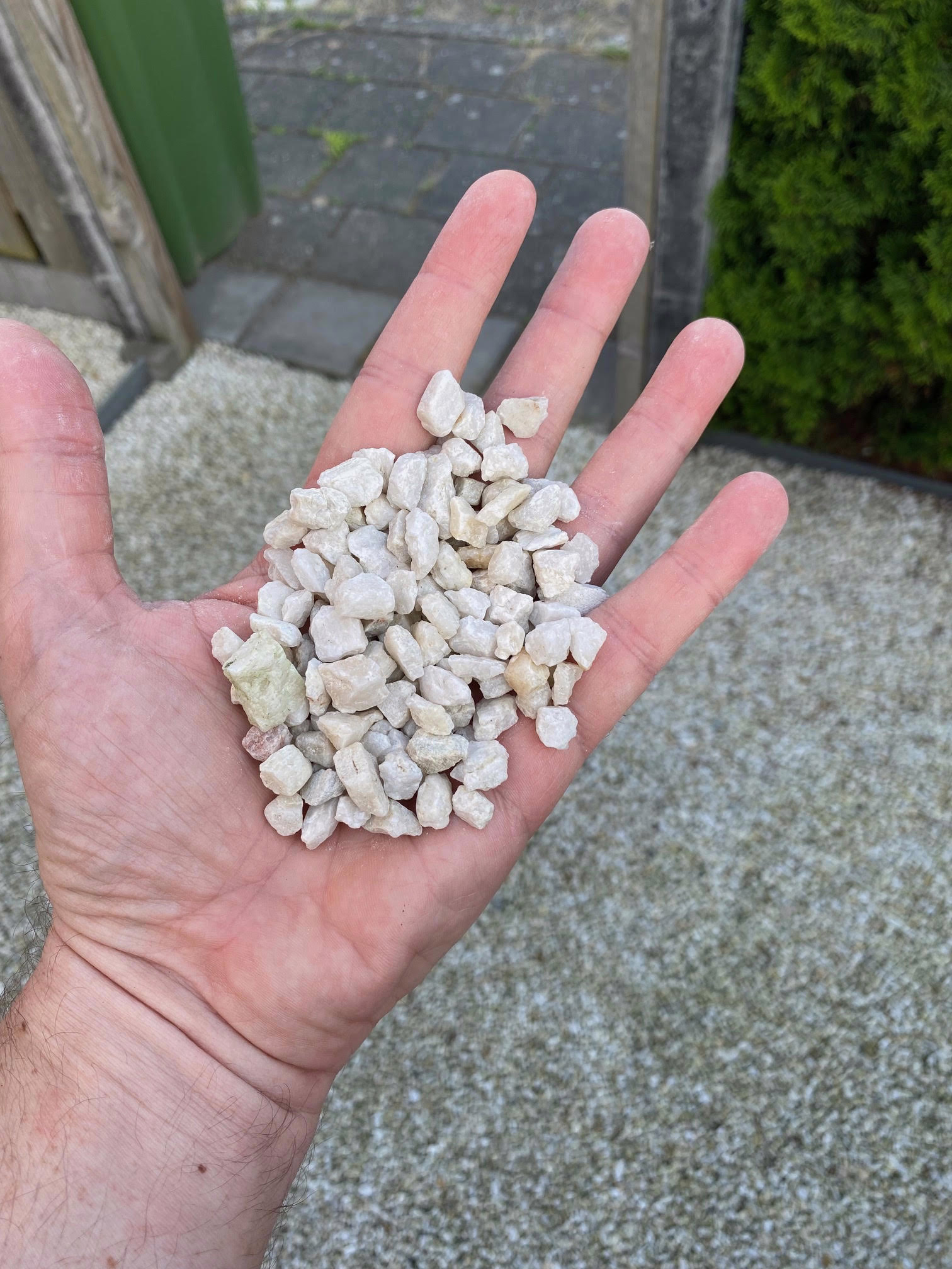 Een hand met witte kwartssplit toont het formaat van de steentjes