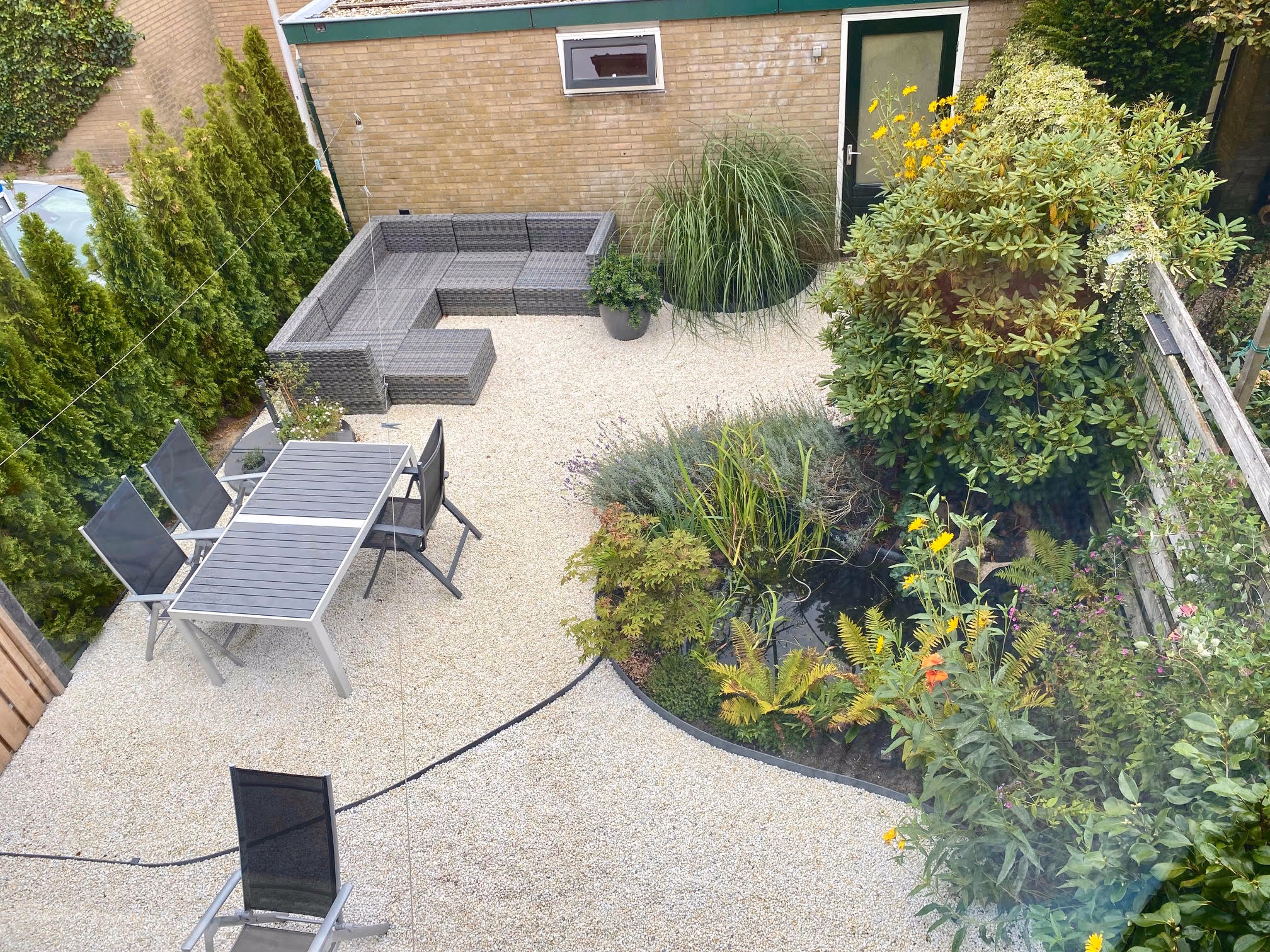 Een tuin met een terras, zithoek, groene borders en witte kwartssplit